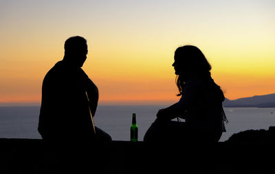 Silhouette of man drinking water from sea during sunset