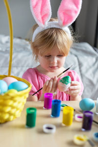 Little girl in easter bunny ears painting colored eggs. easter at home and craft concept.