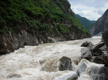Scenic view of waterfall by rocks against sky