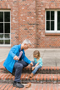 Grandfather and girl sitting against brick wall