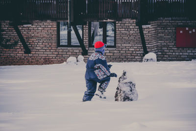Rear view of boy playing on snow covered yard during winter