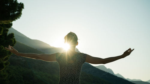 Woman standing with arms outstretched against clear sky