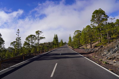 Empty road amidst trees against sky