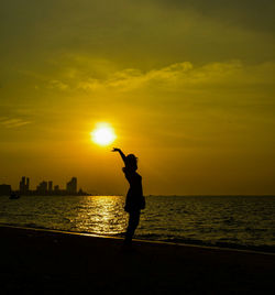 Silhouette person standing by sea against sky during sunset