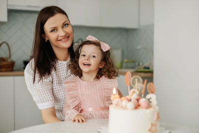 Portrait of a charming mother and daughter with a birthday cake in the kitchen. 