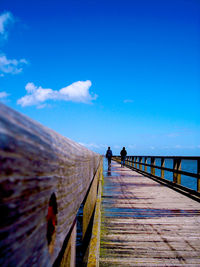 People walking on footpath against blue sky