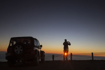 Rear view of silhouette man standing on beach against sky during sunset