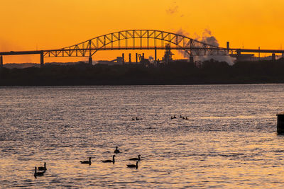 Silhouette bridge over river against sky during sunset