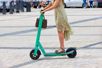 A young woman in a light dress rides a rental electric scooter around the city. 