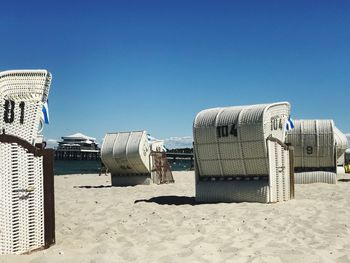 Hooded chairs on beach against clear blue sky