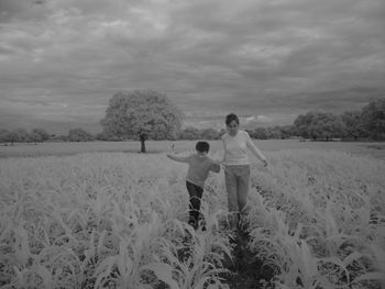Mother and son standing on agricultural field against sky