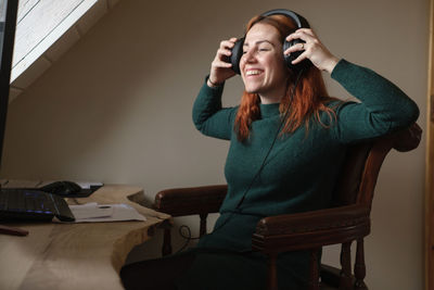 Middle age woman listening to music in big headphones near computer at home. creating play list