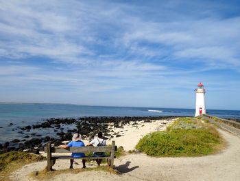 People sitting on bench at beach against sky