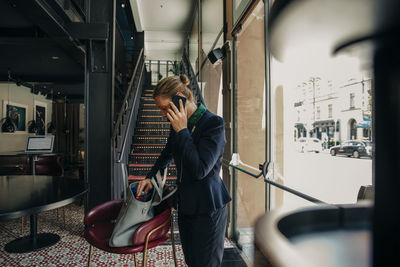 Mature businesswoman talking on smart phone while removing from bag in hotel lounge