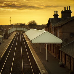 Railroad station platform against sky during sunset