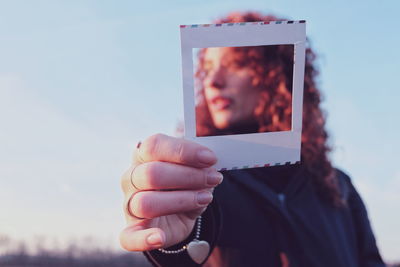 Portrait of woman holding frame against sky