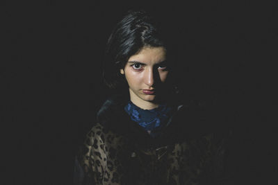 Portrait of young woman standing against black background