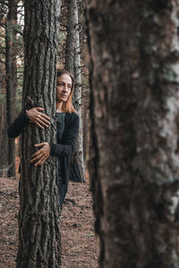 Woman standing by tree trunk in forest