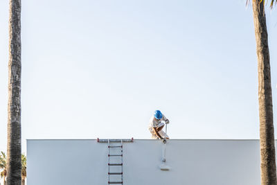 Unrecognizable young painter painting the facade of an apartment with a roller from the roof and the staircase on the side