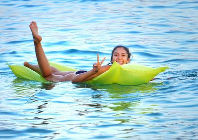 Carefree young woman showing peace symbol while relaxing on floating mattress