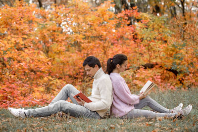 Couple reading books sitting back to back at park