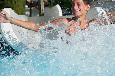 Boy sliding into swimming pool at water park