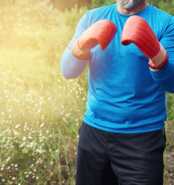 Midsection of man wearing boxing gloves while standing on field