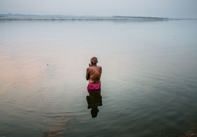 Rear view of shirtless man in sea against sky