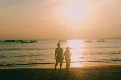 Men standing on beach against sky during sunset