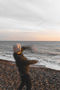 Rear view of woman standing at beach against sky