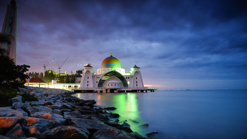 Illuminated building by sea against sky at dusk