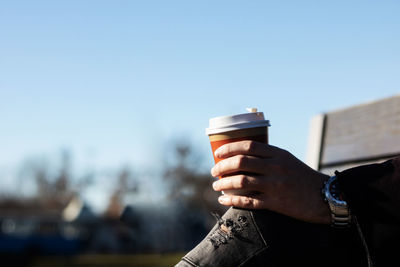 Man holding coffee cup against clear sky