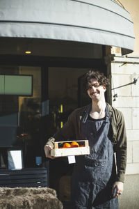 Smiling male entrepreneur with food box standing outside store