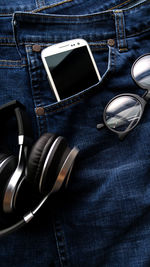 High angle view of headphone and sunglass on jeans