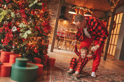 Candid authentic happy dad and son in red plaid pajamas fooling around at wood lodge xmas decorated