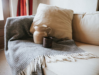 Mug and pitcher near cushion on sofa