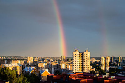 Rainbow over buildings in city against sky