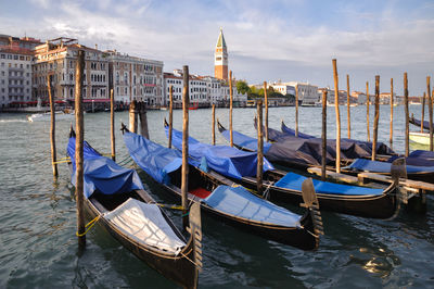 Boats moored in canal by city against sky