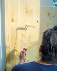 Hand applying clear coat paint on a wooden surface with roller brush. painting wood wall and floor.