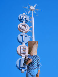 Man wearing paper bag while standing against information sign