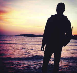 Rear view of silhouette man standing at beach during sunset