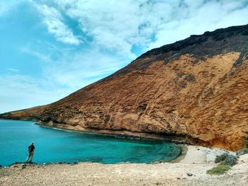 Scenic view of sea by mountain against sky