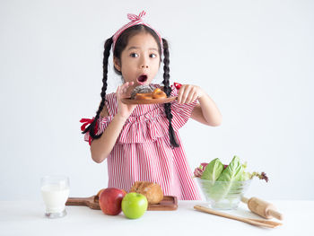 Shocked girl holding pretzel in serving tray against white background