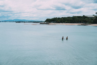 Men in sea against cloudy sky