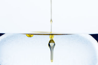 Close-up of water drop hanging from metal against white background