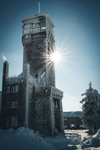 Sun shining over snow covered building against sky