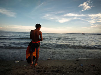 Full length of shirtless man standing on beach against sky during sunset