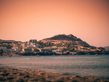 Sea by townscape against clear sky during sunset