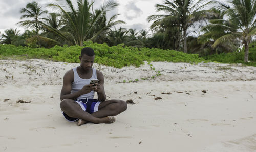 Portrait of young man sitting on sand at beach