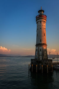 Lighthouse by sea against sky during sunset